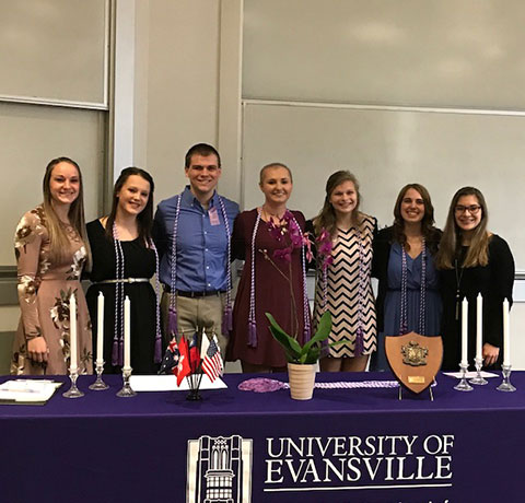 Seven people standing behind a table on which sits a pretty green plant