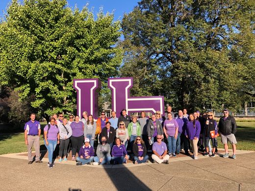 A group of employees in front of the purple letters